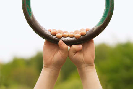 Children's hands are holding onto an old iron gymnastic ring. A little girl's hands are holding onto...