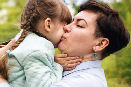 A mother with her eyes closed, kisses her little daughter on the cheek in the open air. A little...