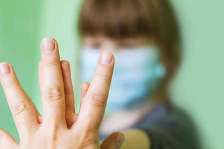 The mother holds the child's hand. A blurry little girl in a medical protective mask holds her...