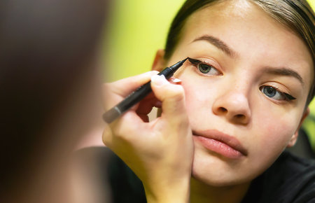 A young woman makes up in the morning, looks in the mirror, paints her eyes with black eyeliner.Charming young teenage girl paints her eyes, makes arrows before a partyの写真素材