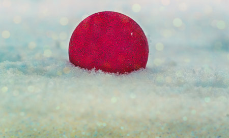 A red New Year's ball lies on the sparkling snow outdoors on a frosty winter day, tinted photo. Space for text. Christmas, festive design.The concept of Christmas and New Year.Bokehの写真素材