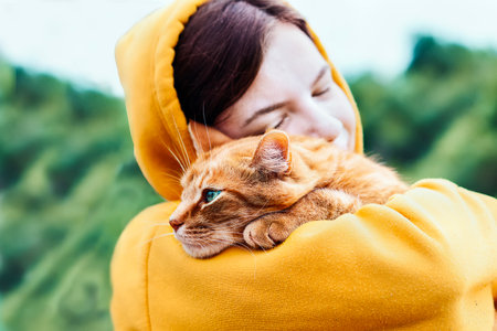 Beautiful pretty girl hugging a cute ginger cat on a blurred background. Close up portrait of a young hipster woman hugging her good friend ginger cat. Relaxation, pleasure. people and animals in loveの写真素材