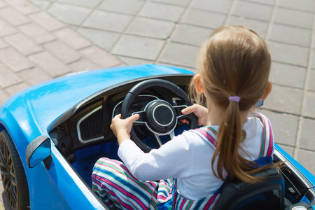 A baby girl is having fun riding a blue electric car in an amusement park. A Cute Little Girl Drives A Children's Car. The concept of a happy childhood. entertainment for children.の写真素材