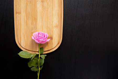 One pink rose lays on a wooden chopping board on a dark background. top view with area for textの写真素材