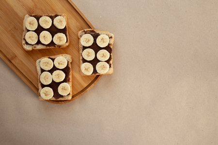 Three banana white bread toasts smeared with chocolate butter that lie on a cutting board on craft paper background. top view with area for textの写真素材