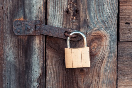 The old and vintage metal padlock with rust on the wooden door, locked for security.の写真素材