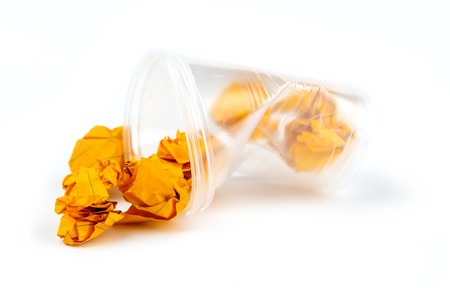 Concept of garbage and pollution. Crumpled plastic cup with orange sheets of paper isolate on white...
