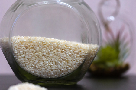 Healthy eating rice groats in a glass jar standing on a table with a green plant on the backgroundの写真素材