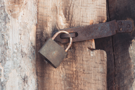 The old and vintage metal padlock with rust on the wooden door, locked for securityの写真素材