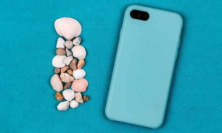 Back side Black Mobile phone or smartphone in aqua blue case on a trendy aqua background with sea shells and space for text.の写真素材