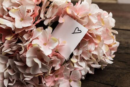 Pastel pink hydrangea flowers and a piece of paper on wood background. Copy space for text.の写真素材