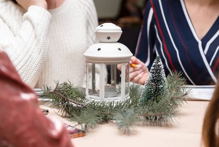 A white metal candlestick with candle inside surrounded with christmas tree. Women sitting around...