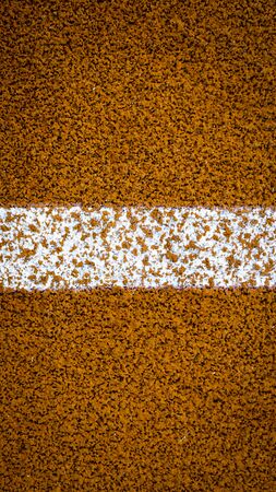 Vertical white dividing strip on orange highway pavement.