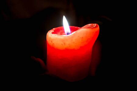 Female hands holding a burning candle in the darkness, hugging it around