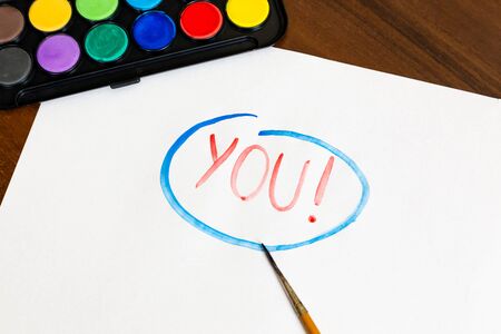 Handwritten YOU text with brush and watercolor paints on white background. Box of watercolor paints with a brush for drawingの写真素材