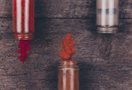 Chilli colorful powder spices scattered from bottle on wooden background