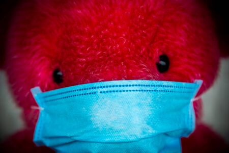 Close up Lonely Red Teddy bear in a protective medical mask on a yellow background with respiratory...