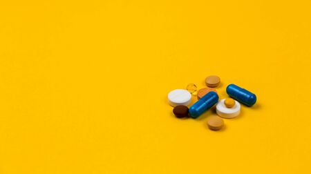 Multicolor tablets and pills capsules from glass bottle on yellow background Health care Close-up Horizontal banner Copy space. Coronavirus covid-19 conceptの写真素材
