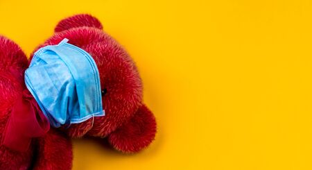Lonely Red Teddy bear in a protective medical mask on a yellow background with respiratory masks. Coronavirus covid-19 prevention concept.の写真素材