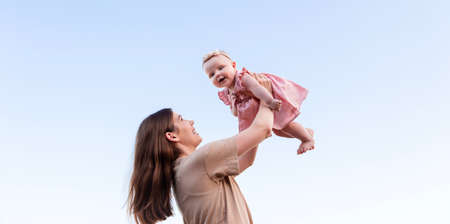 Young mother throws up baby daughter and laughing in the sky. Happy family in the summer outdoorsの写真素材