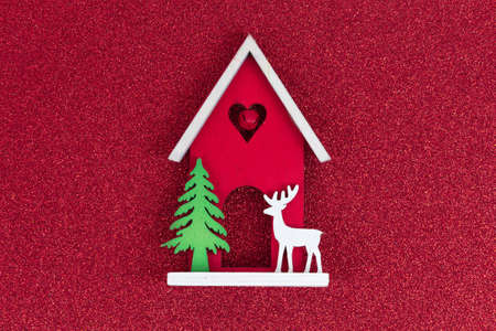 Christmas flatlay layout. wooden toy house, a deer and a Christmas tree on a red glitter shiny background. Christmas card with place for textの写真素材