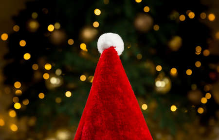 Santa hat on the background of a Christmas tree and garlands. Close-up Christmas concept red hat on bokeh background of glowing garlandsの写真素材
