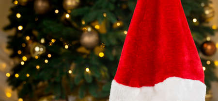 Santa hat on the background of a Christmas tree and garlands. Close-up Christmas concept red hat on bokeh background of glowing garlandsの写真素材