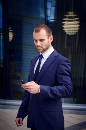 Businessman touching smart phone standing outside business centerの写真素材