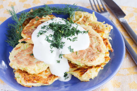 fried zucchini fritters with sour cream and dill on a plate