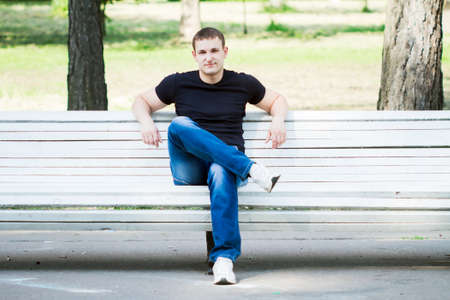 The young man sits on a bench in parkの写真素材