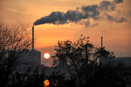 Horizon industry in a small netherland town in Europe, with a big chimney and smoke, sunset and sun as backgroundの写真素材
