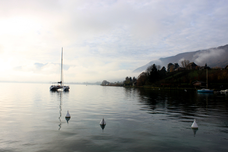 Blue lake of annecy with a parade of couple of grebes and mountains on winter morning.の写真素材