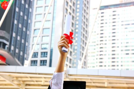 the graduate holding her graduation certificate over head  and very happy  in her success.の写真素材