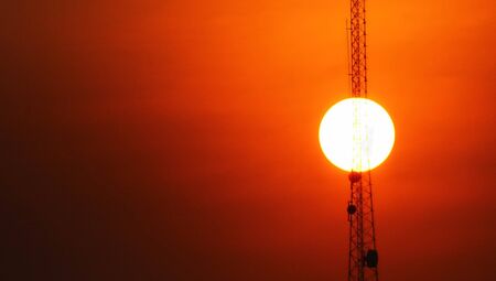 the telacommunication pole with sunset sky background. blured  silhouette electric workers working on high ground with safety uniform.の写真素材