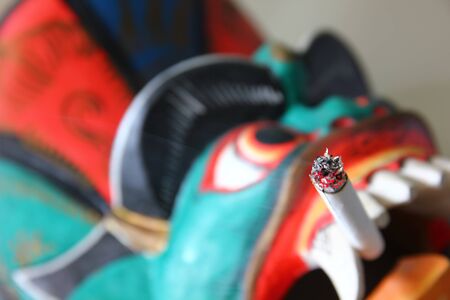 close up the multicolor devil mask smoking cigarette.の写真素材