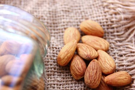 close up roasted organic brown almond seed  on sack floor  and  some of almond in the  square bottle.の写真素材