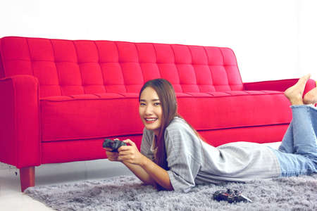Asian young woman listening love music  from  head phone and online by laptop ,relax  on gray carpet red sofa backgroundの写真素材