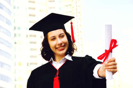 graduate student wearing robe in moment happy showing diploma in her hand after gradution ceremonyの写真素材