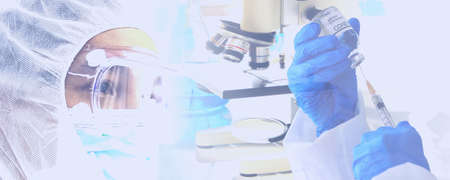 the doctor in protective virus suit looking corona virus vaccine in hand with microscope lab equipment backgroundの写真素材