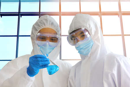 doctors in virus protective suit working in lab looking the example in glass bottleの写真素材