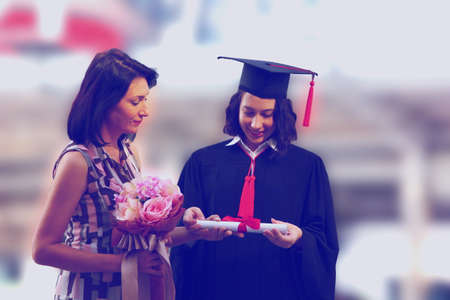 happy adult woman with  teen girl in graduation gown pride with  diploma in hand on graduation day