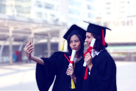 happy young couple in graduation gown enjoy  to selfie in graduation dayの写真素材