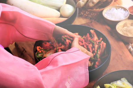 top view Korean woman in hanbok national costume cooking kimchi in black ceramic bowlの写真素材