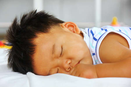 Asian baby lying on bed sheet . kid happy sleep after eat , close upの写真素材