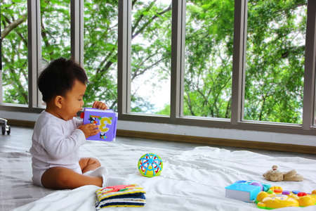 Asian baby playing with colorful toy box and licking the toy in hand