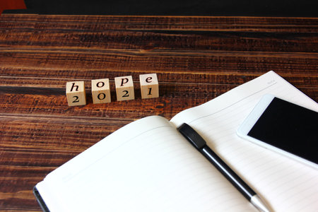the number 2021 with letter hope on wooden cube with pen and smart phone on note book, good year for business . business conceptの写真素材