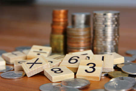 text number on wood cube with blur coins stacking on wood floor. the managing money daily spending...