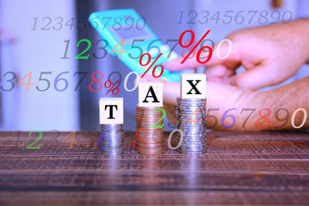 text TAX on wood cube on coins stacking with blur hand using calculator and illustration of number % sign ,business conceptの写真素材