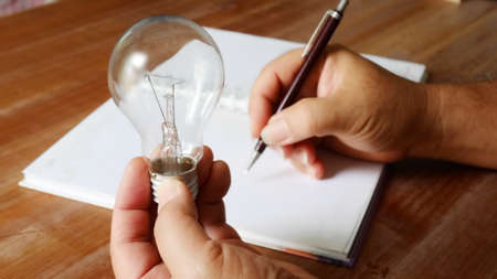 worker holding light bulb in left hand and using right hand recoarding the good idea