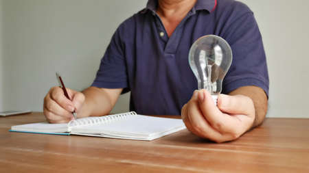 worker holding light bulb in left hand and using right hand recoarding the good ideaの写真素材